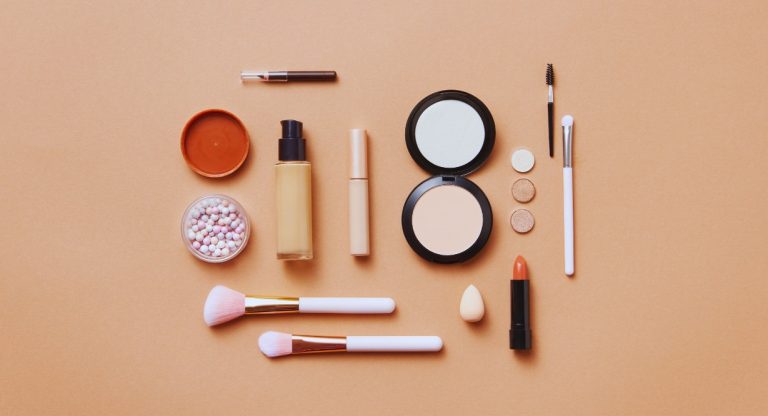Produits de maquillage, poudres et pinceaux disposés sur fond beige