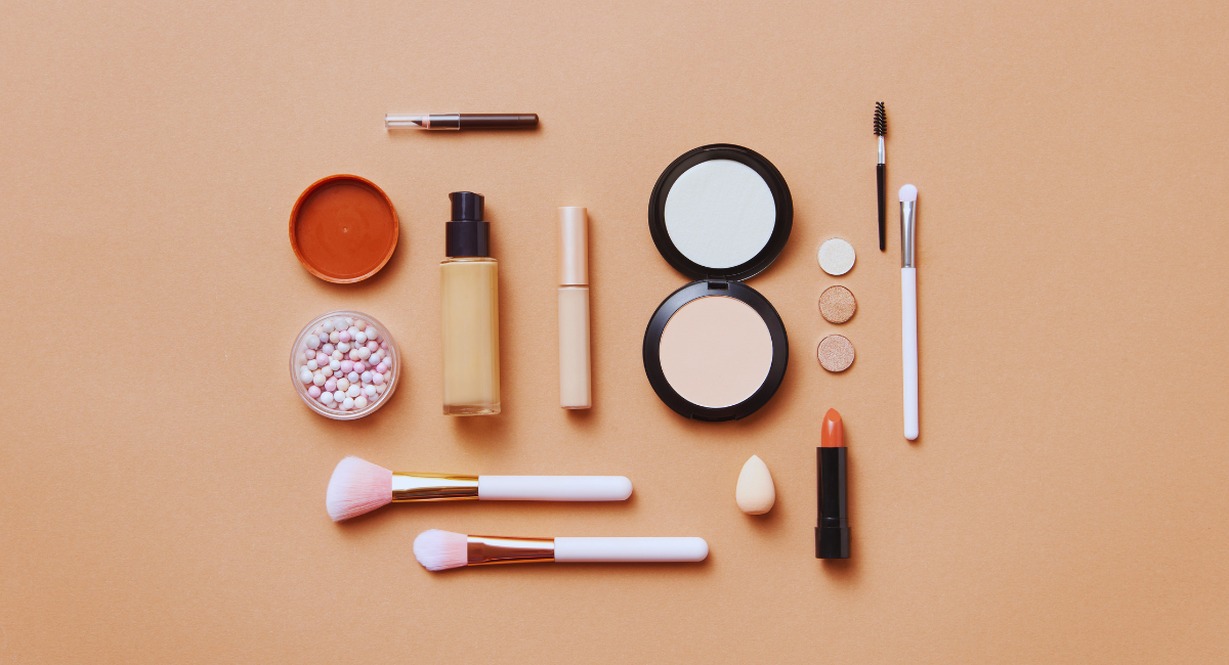 Produits de maquillage, poudres et pinceaux disposés sur fond beige