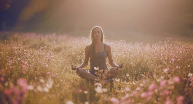 Femme méditant dans un champ de fleurs à la lumière du lever du soleil
